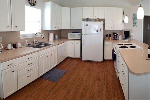 A modern kitchen with white cabinets, a stainless steel sink, a microwave, a refrigerator, and a stove.