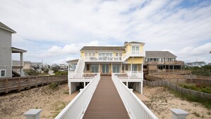 Una propiedad frente a la playa con un paseo marítimo de madera que conduce a un edificio de varios pisos con balcones.