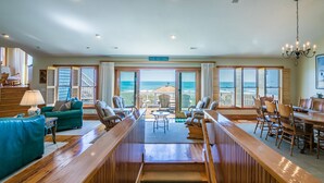 Una habitación amplia con un largo banco de madera, sofás de cuero verde y un comedor con sillas de madera.