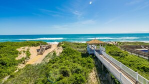 Vista de la playa con un paseo de madera que lleva a un mirador sobre el océano.