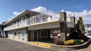 A two-story motel with a balcony on the upper floor, stone pillars, and a landscaped garden area.