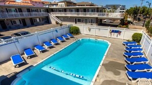 A rectangular swimming pool with blue lounge chairs and a white fence surrounding it.
