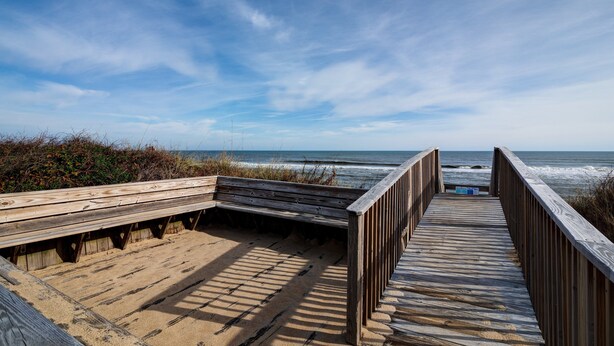 Pasarela de madera que lleva a la playa, con un banco y un cartel.