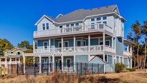 Une maison à deux étages avec un balcon à l’étage supérieur, une véranda couverte au rez-de-chaussée et une cour clôturée.