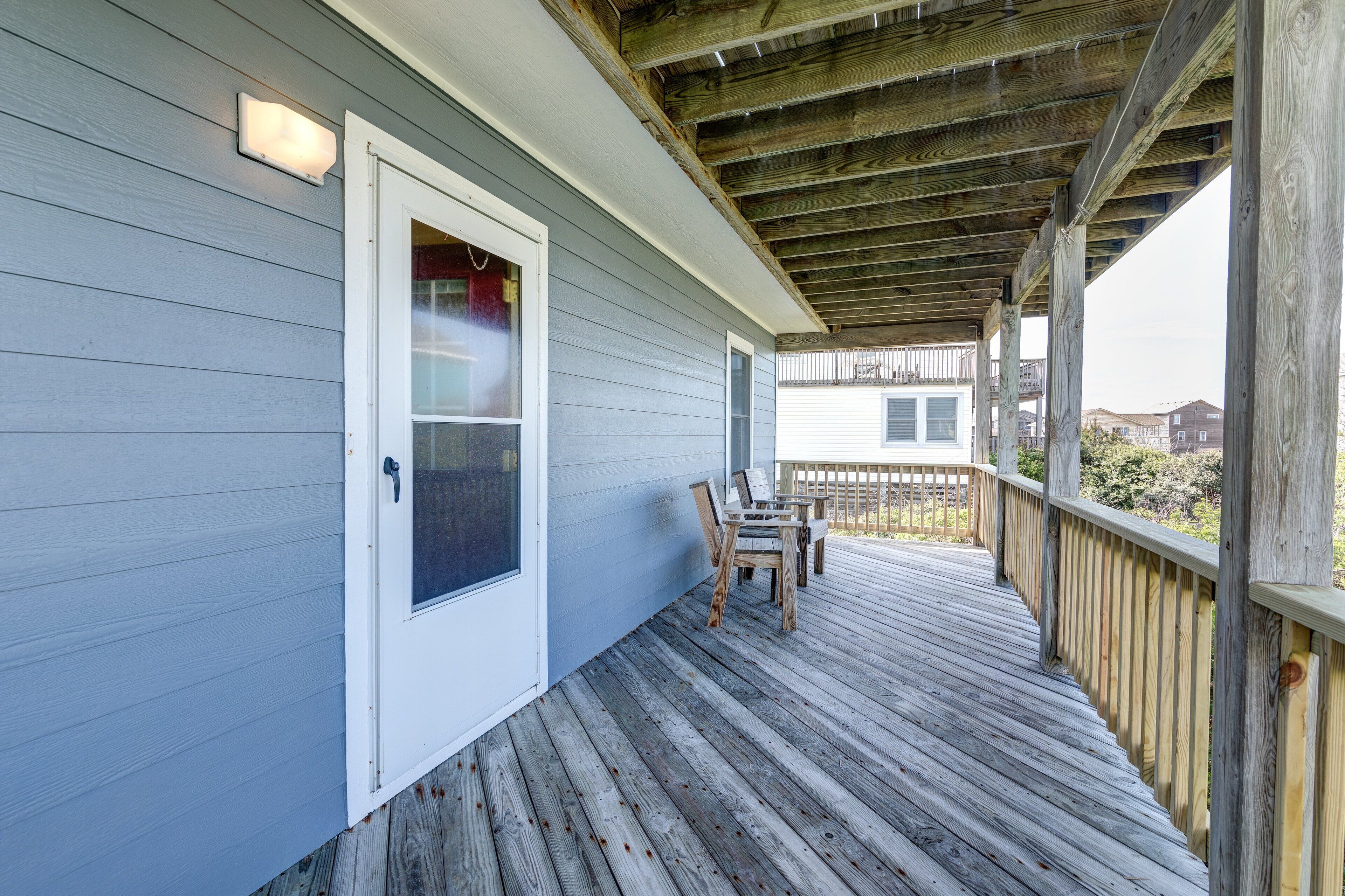 A covered porch with a wooden deck, a door with a window, and a view of neighboring houses.
