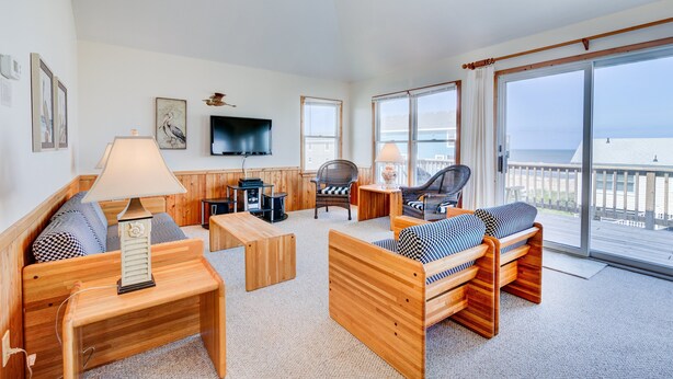 A spacious room with a wooden bed, a sofa, a chair, and a TV mounted on the wall. - 6285-Tidal Song, | Oceanside | South Nags Head | Sleeps 8 (Nags Head)