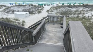 Una pasarela de madera que lleva a una playa con sombrillas y sillas reclinables.