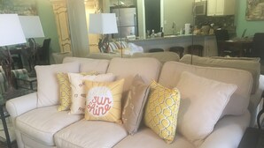 Una sala de estar con un sofá color beige, cojines estampados y un comedor con sillas y una mesa.