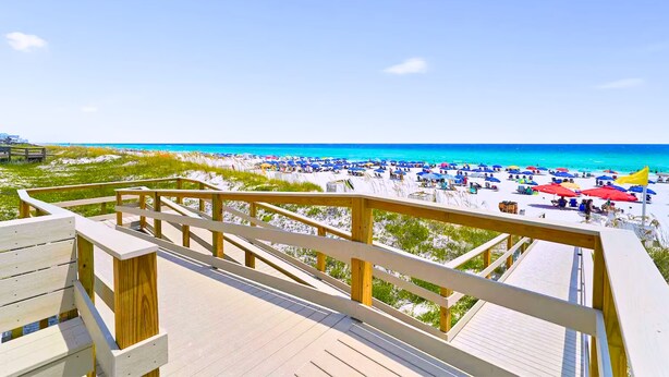 A wooden deck with a view of a beach with umbrellas and people.