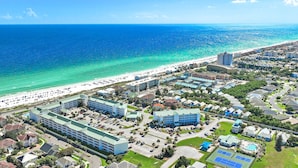 An aerial view of a coastal resort area with a beachfront, hotel buildings, and a swimming pool.