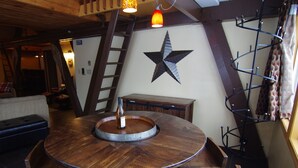 A round wooden table with a bottle of wine, surrounded by wooden chairs, in a room with exposed wooden beams and a star decoration on the wall. - A Loft Above, Ski in/out, 3 Lofts, Private Hot Tub (Vernon)