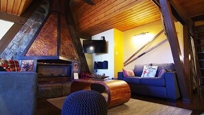 A cozy loft-style living space with a stone fireplace, a blue sofa, and a wooden ceiling fan. - A Loft Above, Ski in/out, 3 Lofts, Private Hot Tub (Vernon)