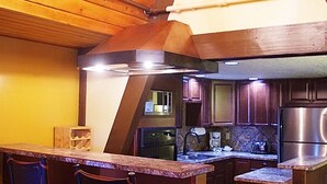 A kitchen with wooden cabinets, a stainless steel refrigerator, and a bar area with stools. - A Loft Above, Ski in/out, 3 Lofts, Private Hot Tub (Vernon)