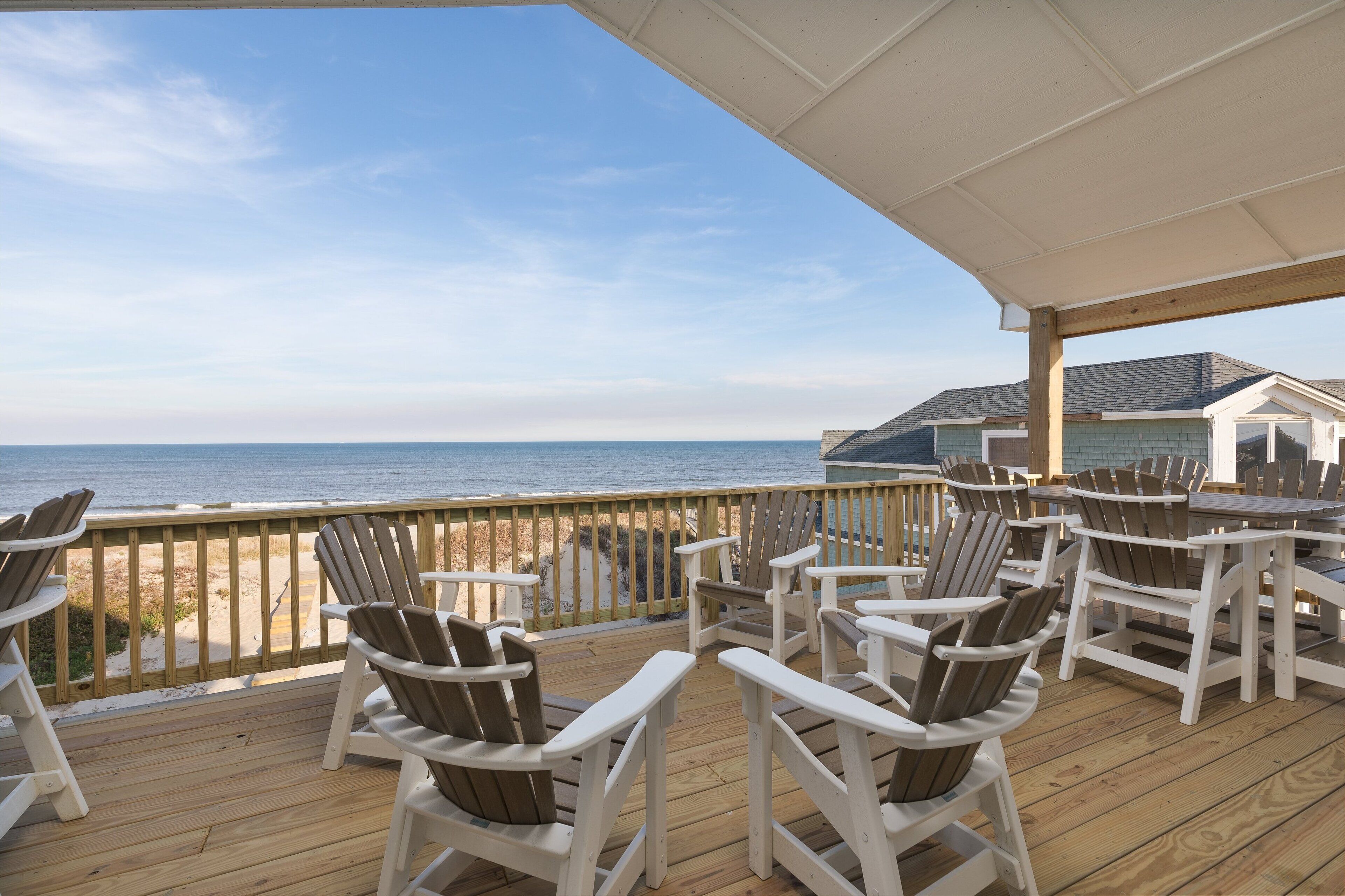 A wooden deck with Adirondack chairs overlooking the beach.