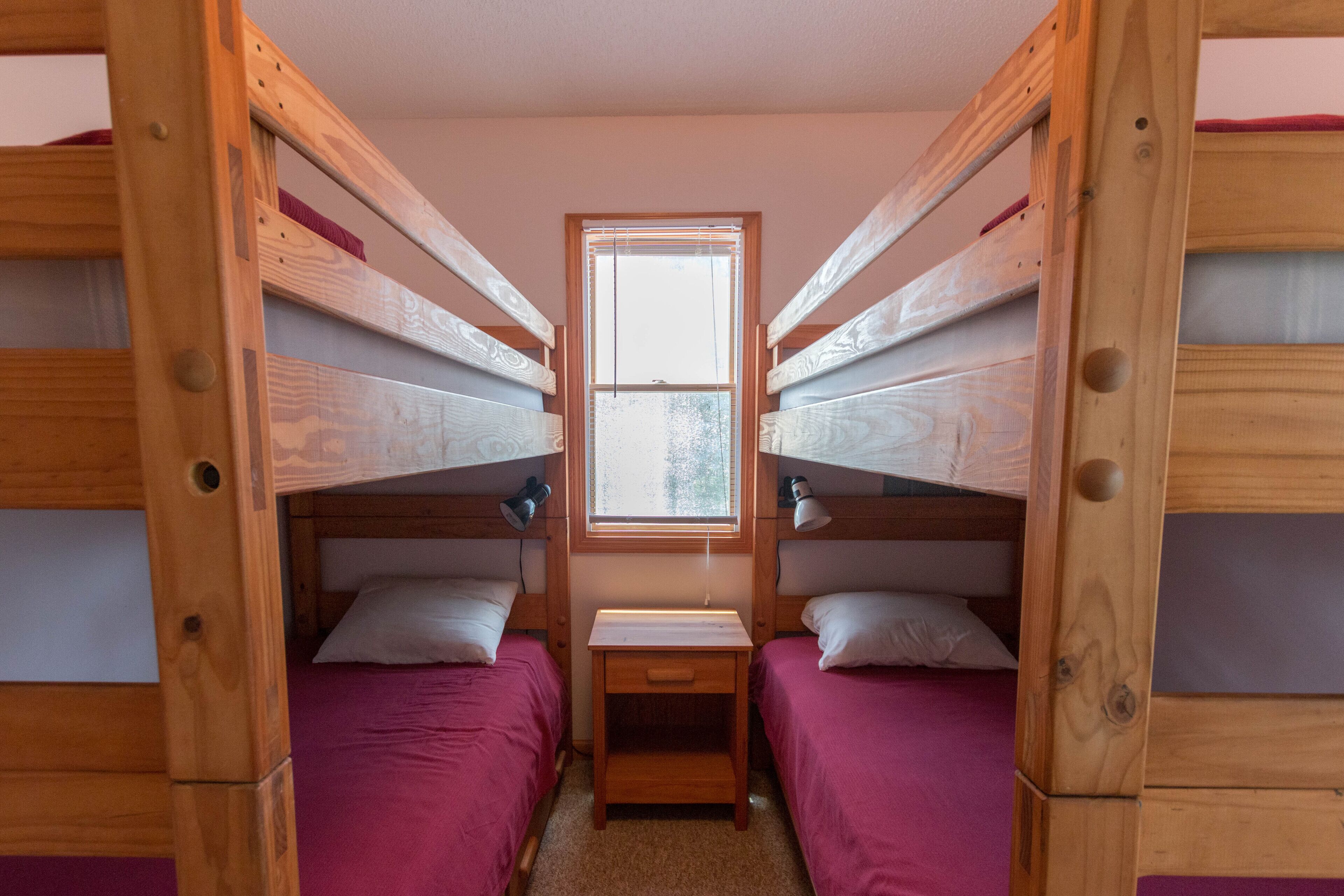 Una habitació amb dos llits superposats, una petita taula de nit de fusta i una finestra.
