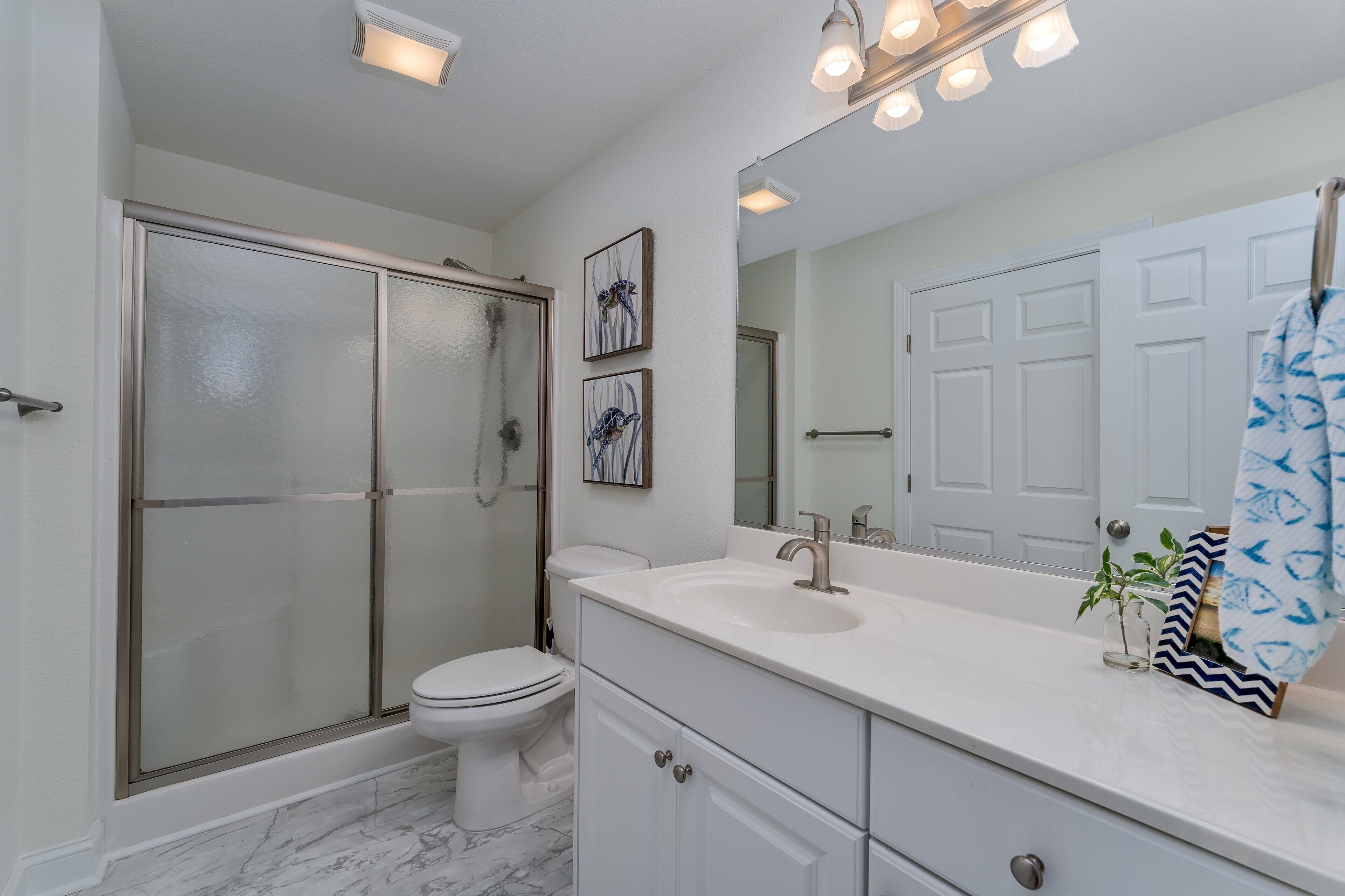 A modern bathroom with a glass-enclosed shower, a white toilet, a large mirror, and a white vanity with a sink.