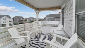 Ein überdachter Balkon mit weißen Adirondack-Stühlen und einem Schachbrettfußboden, mit Blick auf ein Wohngebiet.