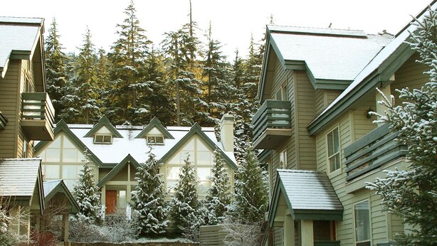 Una hilera de edificios tipo chalet con techos pronunciados, rodeados de árboles cubiertos de nieve y un camino pavimentado.