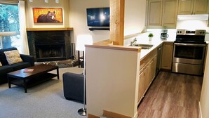 Una sala de estar moderna con chimenea, un sofá y una mesa de centro. Hay una zona de cocina con estufa, fregadero y armarios.