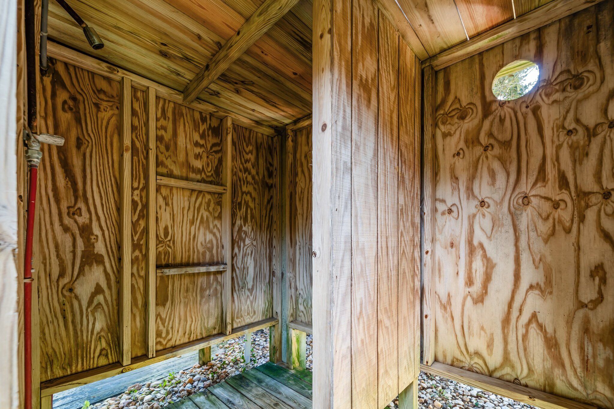 Interior de una cabaña de madera con techo inclinado, paredes de madera y una pequeña ventana circular.