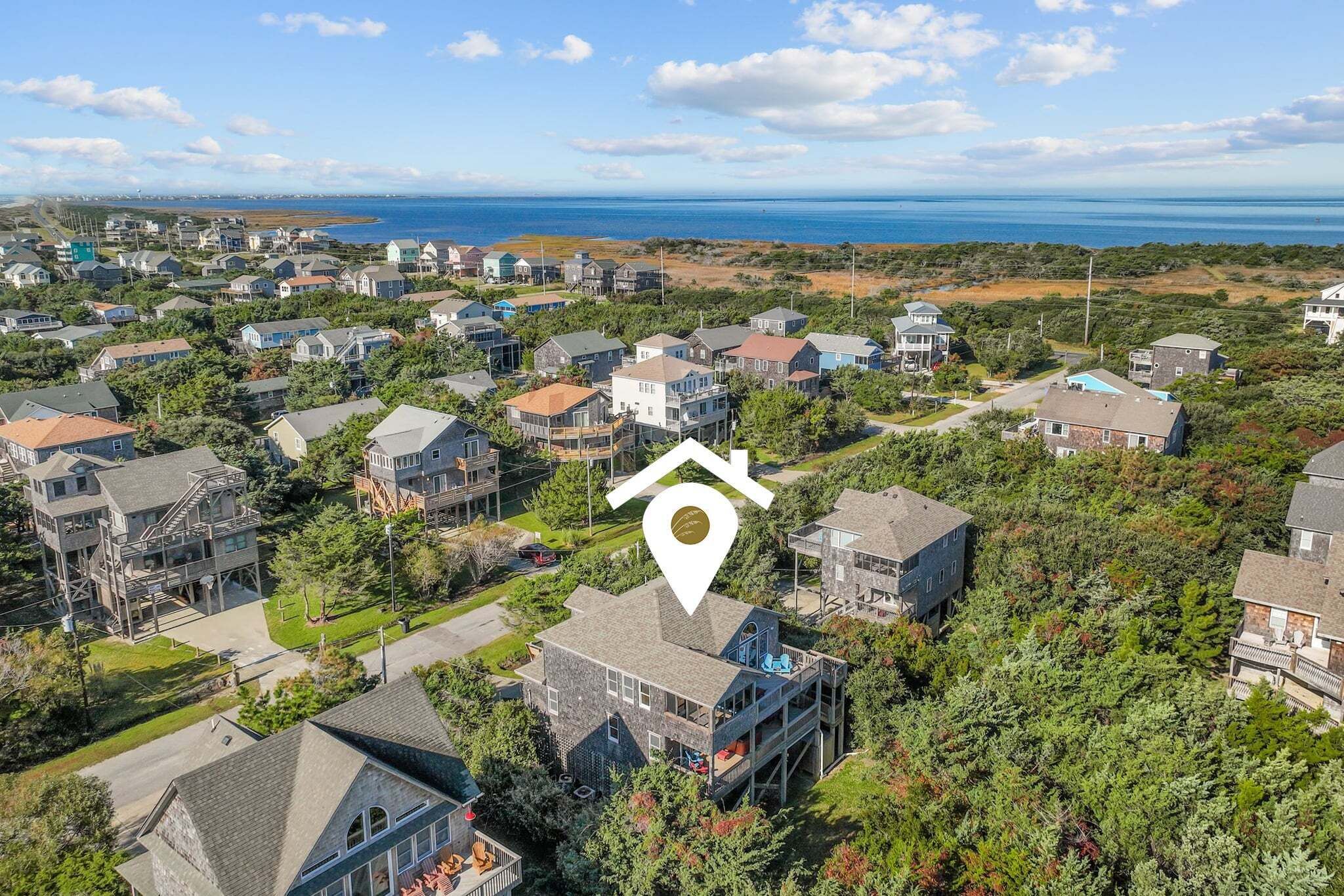 A residential area with houses, a prominent house with a balcony, and a view of the ocean.