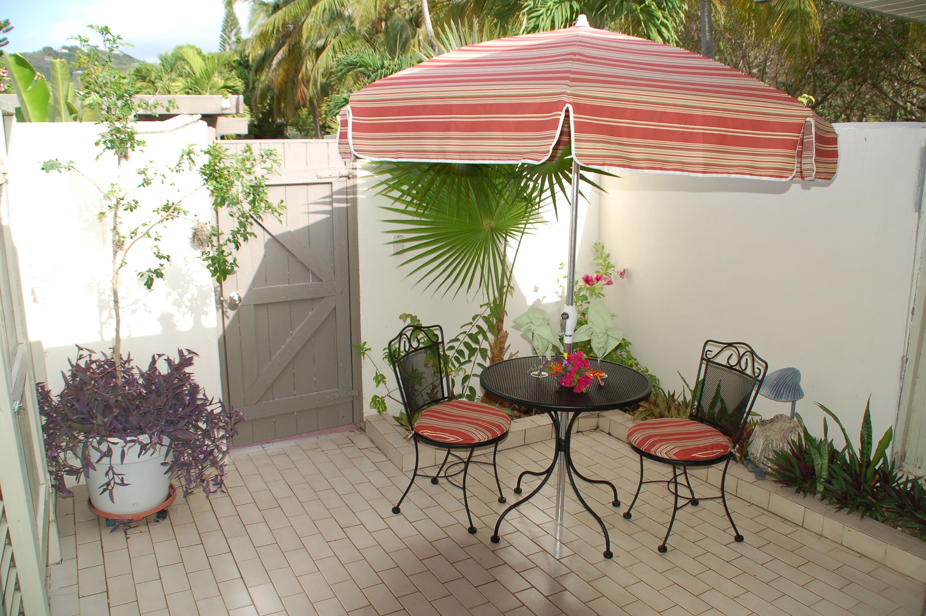 An outdoor patio with a table and two chairs, a striped umbrella, and potted plants.