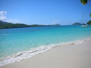 A beach with clear turquoise water, a sandy shore, and boats in the distance. - 150 footsteps to the beach (Estate Smith Bay)