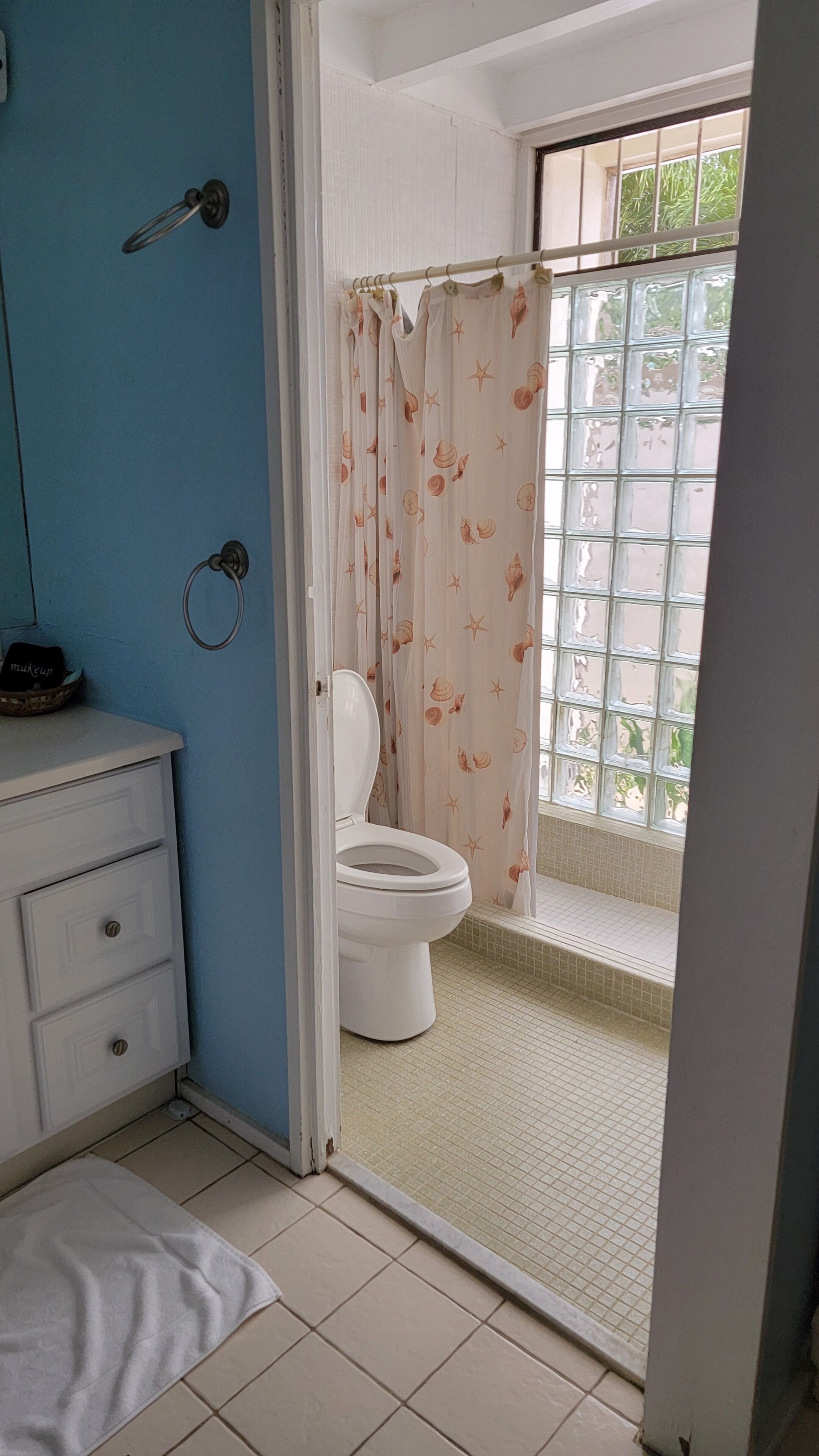 Un baño con inodoro, un lavabo con cesta y cortina de ducha con estampado de conchas.