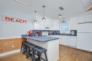 Eine moderne Küche mit weißen Schränken, einer blauen Arbeitsplatte und einem Holzboden. Auf der Arbeitsplatte befinden sich drei Pendelleuchten, eine Mikrowelle und eine Kaffeemaschine.