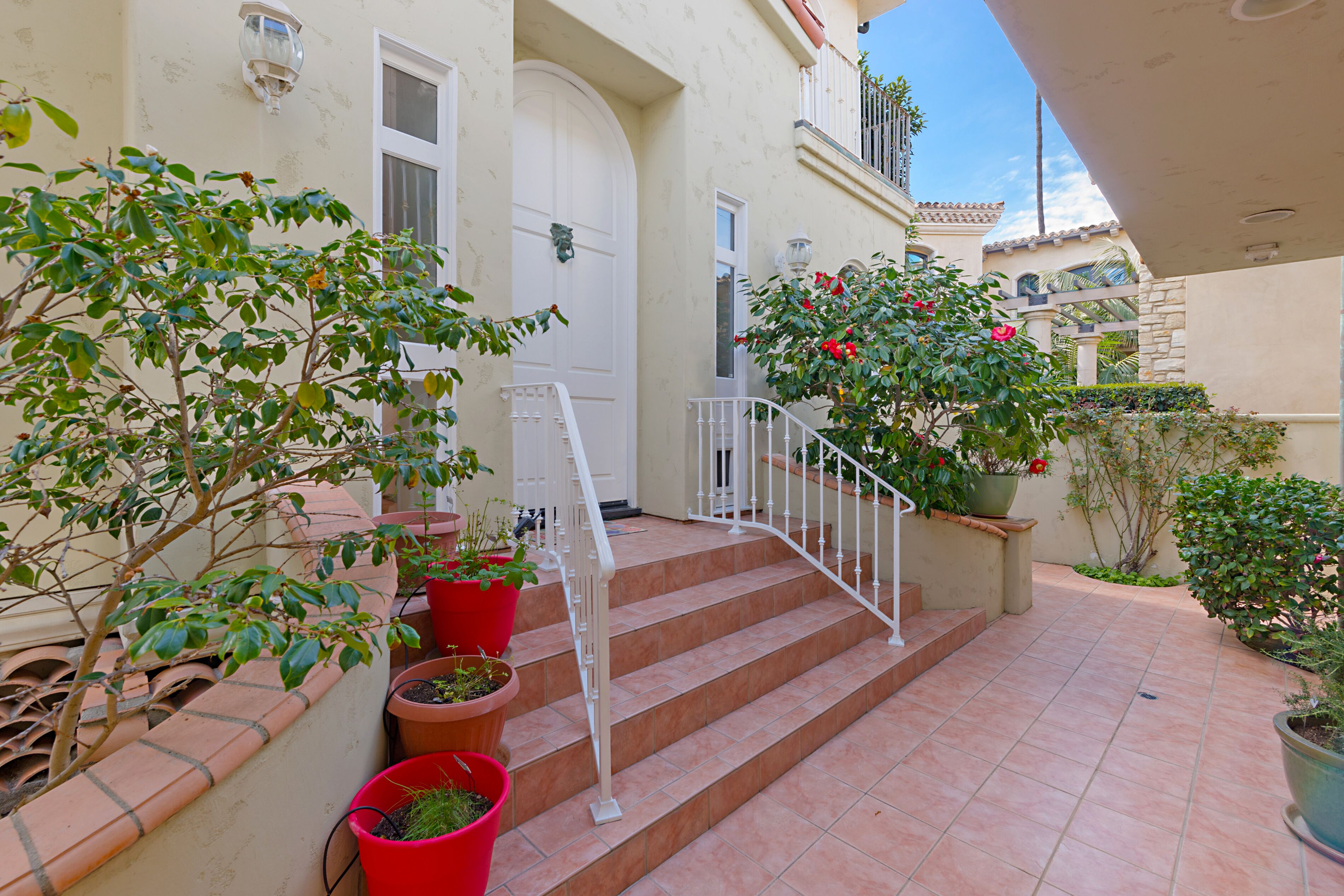 A residential building with a white door, a set of stairs with a white railing, and potted plants.