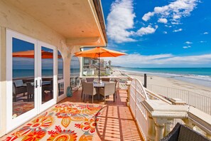 A balcony with a view of the beach, outdoor furniture, and a patterned floor.