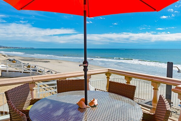 A balcony with a table and chairs overlooking a beach.