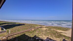 Ein Küstenblick mit einer Holzpromenade, die zum Strand führt, grasbewachsenen Dünen und dem Meer.