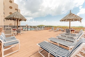 Relax on the sun deck with lounge chairs and a pool table, shaded by thatched umbrellas.