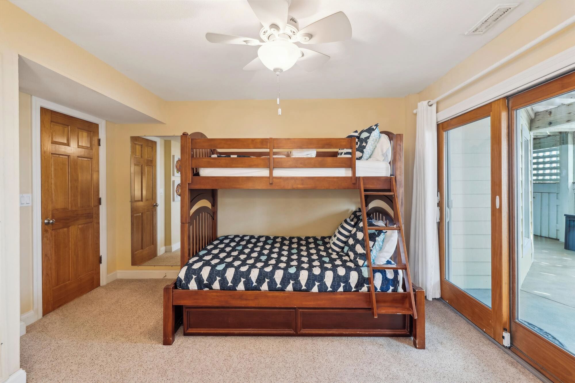 A bunk bed room with a ceiling fan, wooden door, and a view through a glass door.
