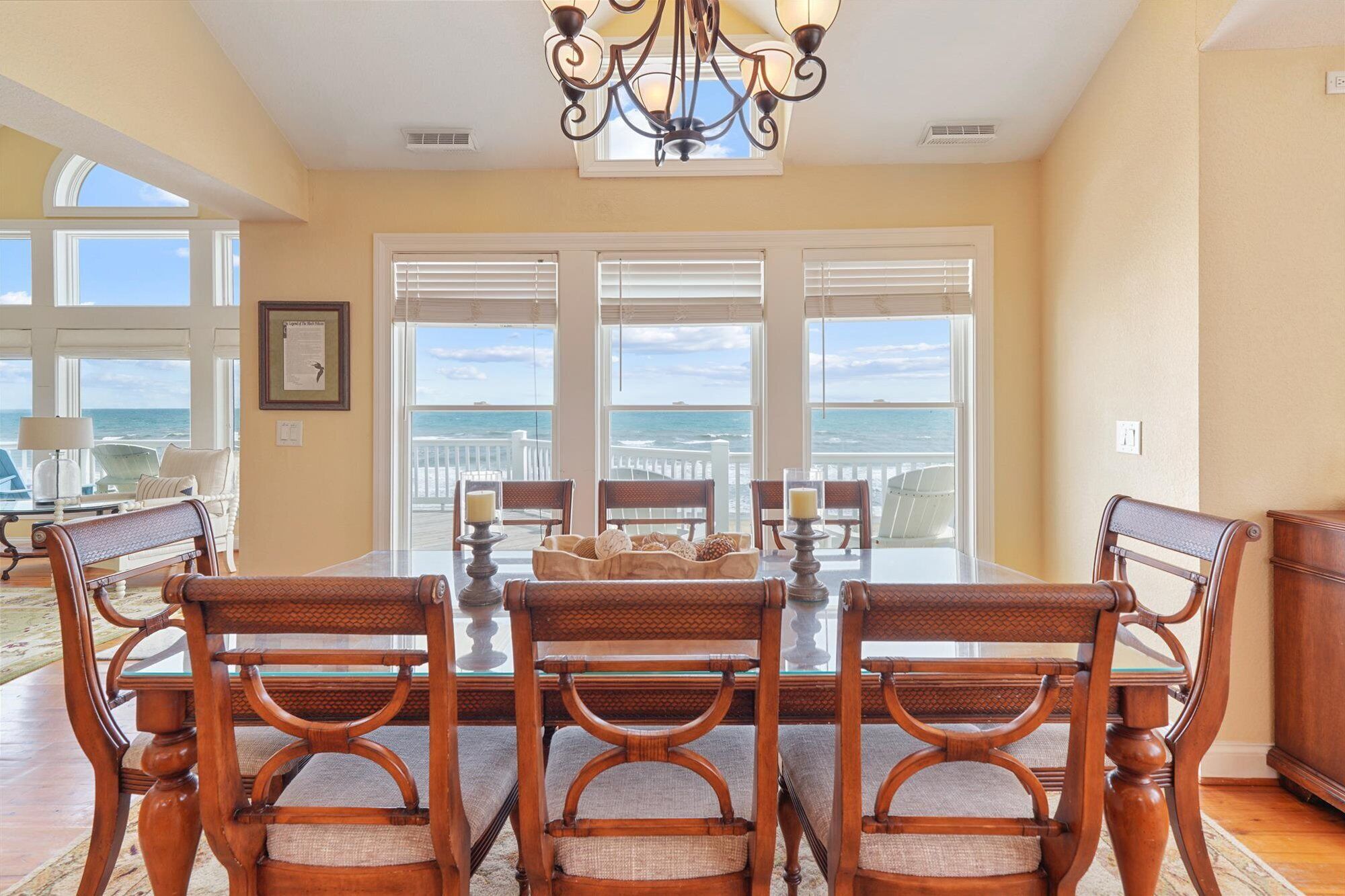 A dining area with a table and chairs, large windows with ocean views, and a chandelier.