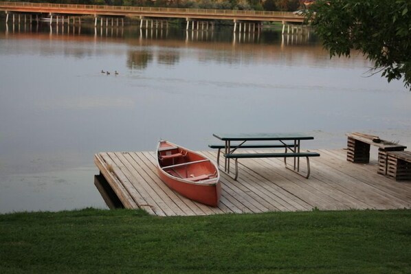 Un muelle de madera con un bote y una mesa de picnic junto a un lago tranquilo.