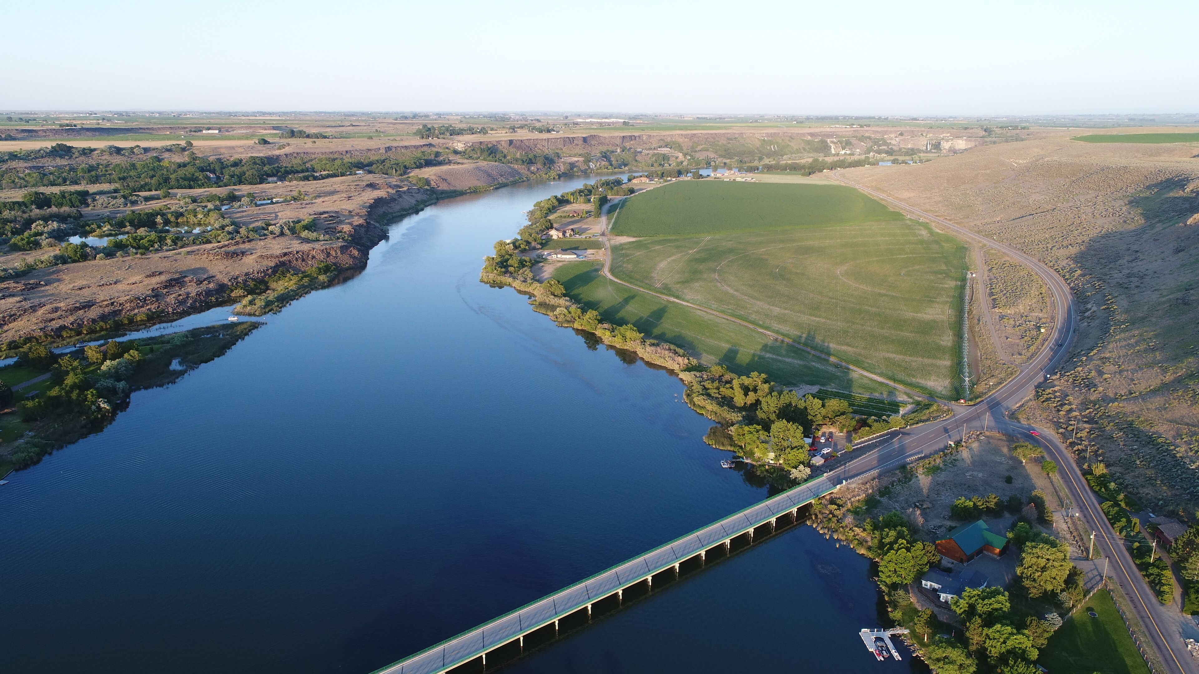 An aerial view of a river with a bridge, fields, and a road.