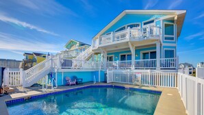 A multi-story building with a swimming pool, white railings, and a clear blue sky.