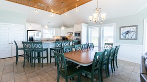 A spacious kitchen with a central island, white cabinetry, and a dining area with green chairs. - 5728- Wench's Pad - Semi-Oceanfront Nags Head | Pool & Hot Tub (Nags Head)