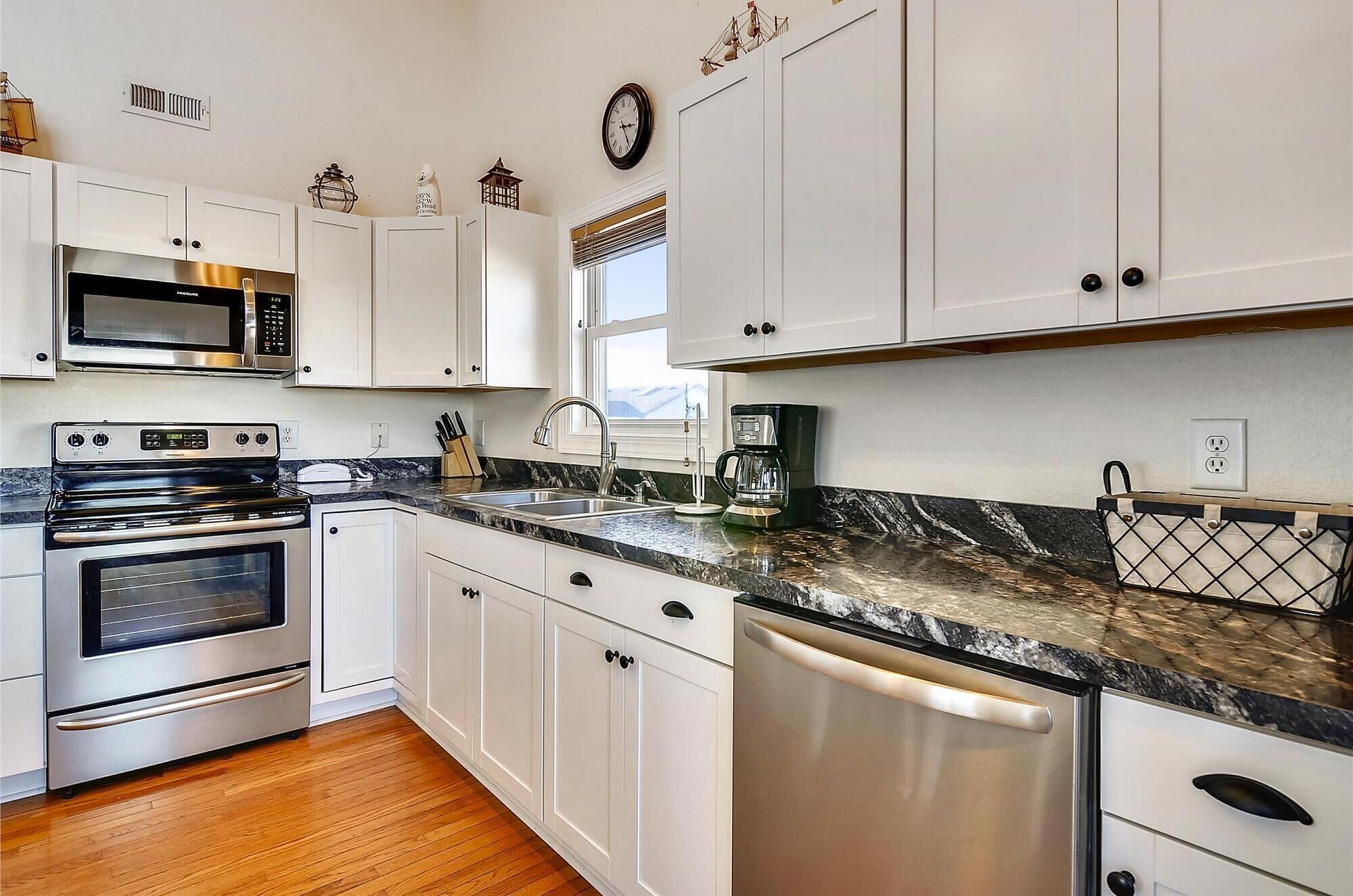 A modern kitchen with white cabinets, stainless steel appliances, and a marble countertop.