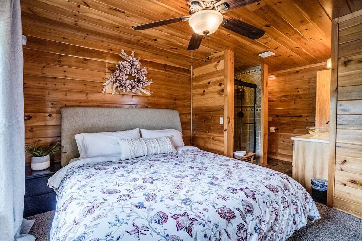Une chambre dans une cabane en bois, avec un lit, un ventilateur de plafond et un élément décoratif mural.
