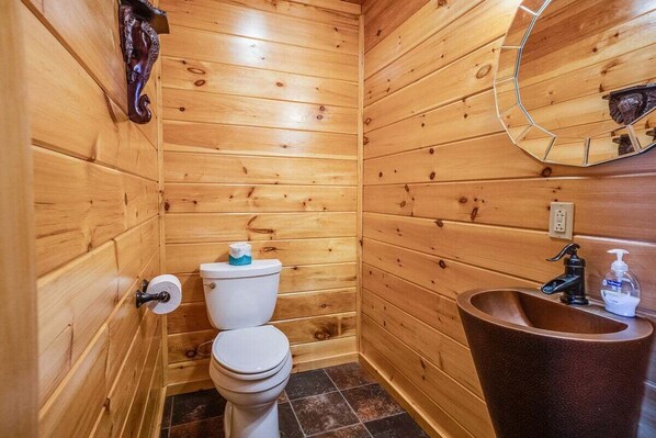 Een badkamer met houten lambrisering, een toilet, wastafel en spiegel.