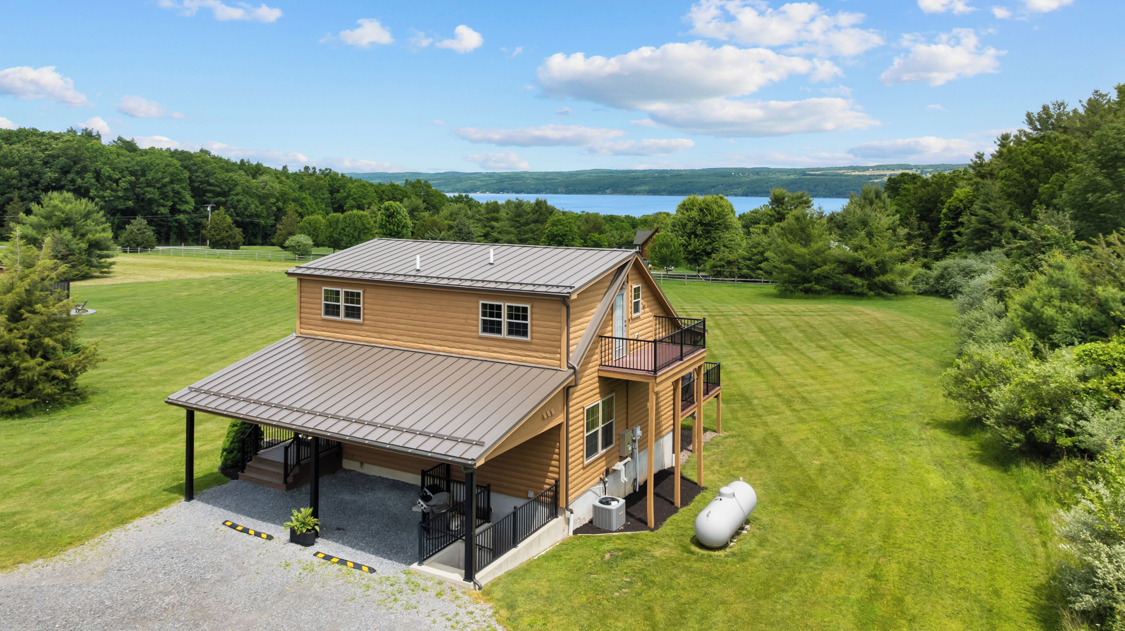 A two-story wooden cabin with a covered porch and a balcony, surrounded by a well-maintained lawn and a lake view.