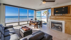 Ein geräumiges Wohnzimmer mit großem Fenster zum Strand, einem Kamin und einem Fernseher.