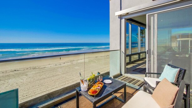 Ein Balkon mit Tisch, gedeckt für eine Mahlzeit, mit Blick auf einen Strand.