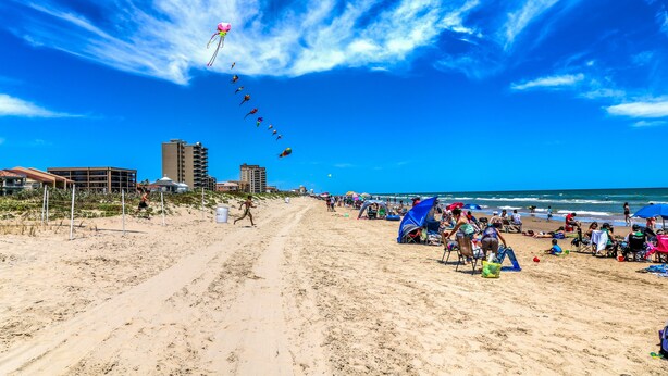 A beach with a clear sky, sandy shore, and buildings in the background.