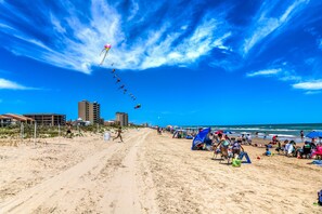 Una playa con cielo despejado, orilla arenosa y edificios al fondo.