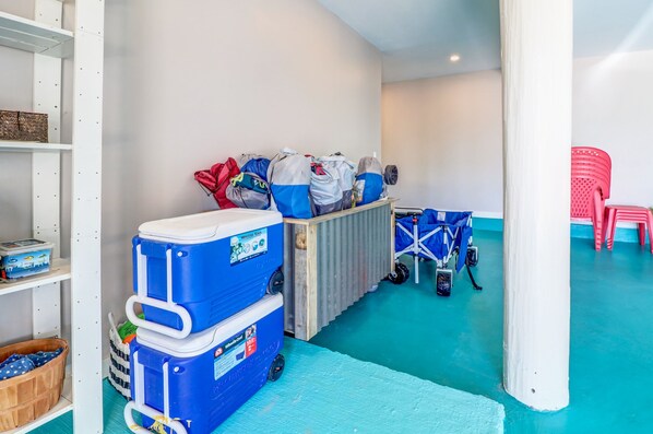 Una habitación con piso azul, paredes blancas y un pilar blanco. Hay contenedores azules para guardar cosas, una silla roja y un carrito azul para bebé.