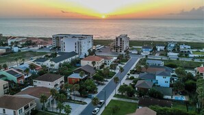 A coastal residential area with modern houses, a clear view of the ocean, and a sunset.